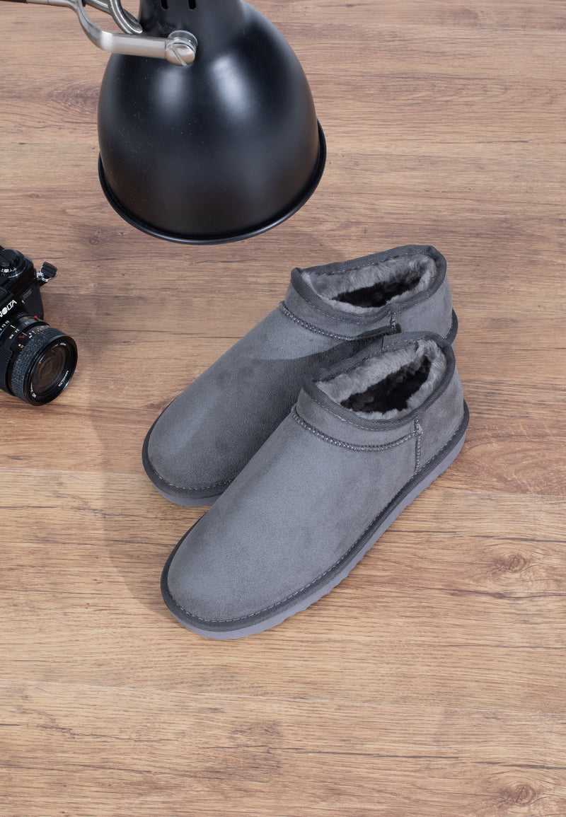 Chaussons fourrés Francis gris vus de dessus, posés sur un parquet près d'une lampe