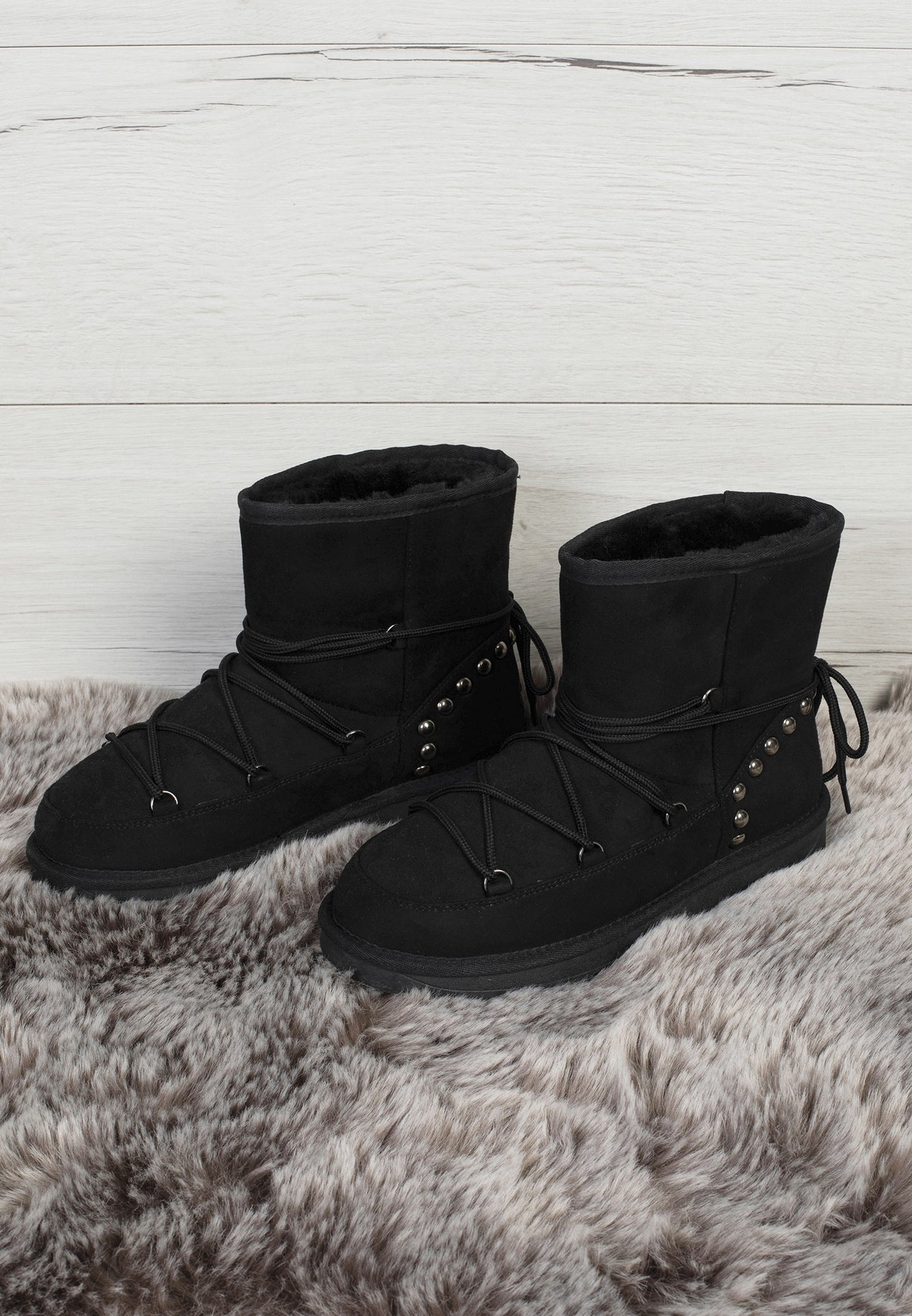 Paire de bottines fourrées Aine noires posées sur un tapis à poils longs, laçage croisé