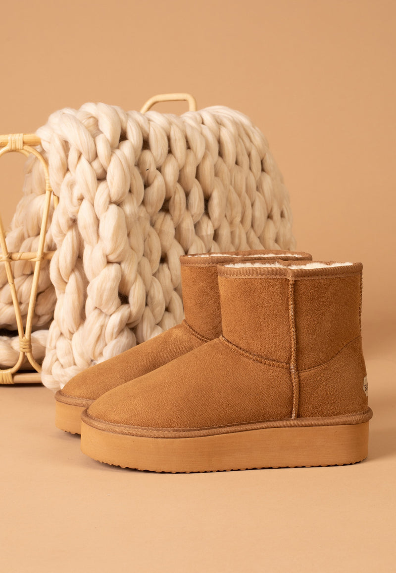 Bottines fourrées Princesse camel posées de trois-quarts devant un plaid en grosse maille