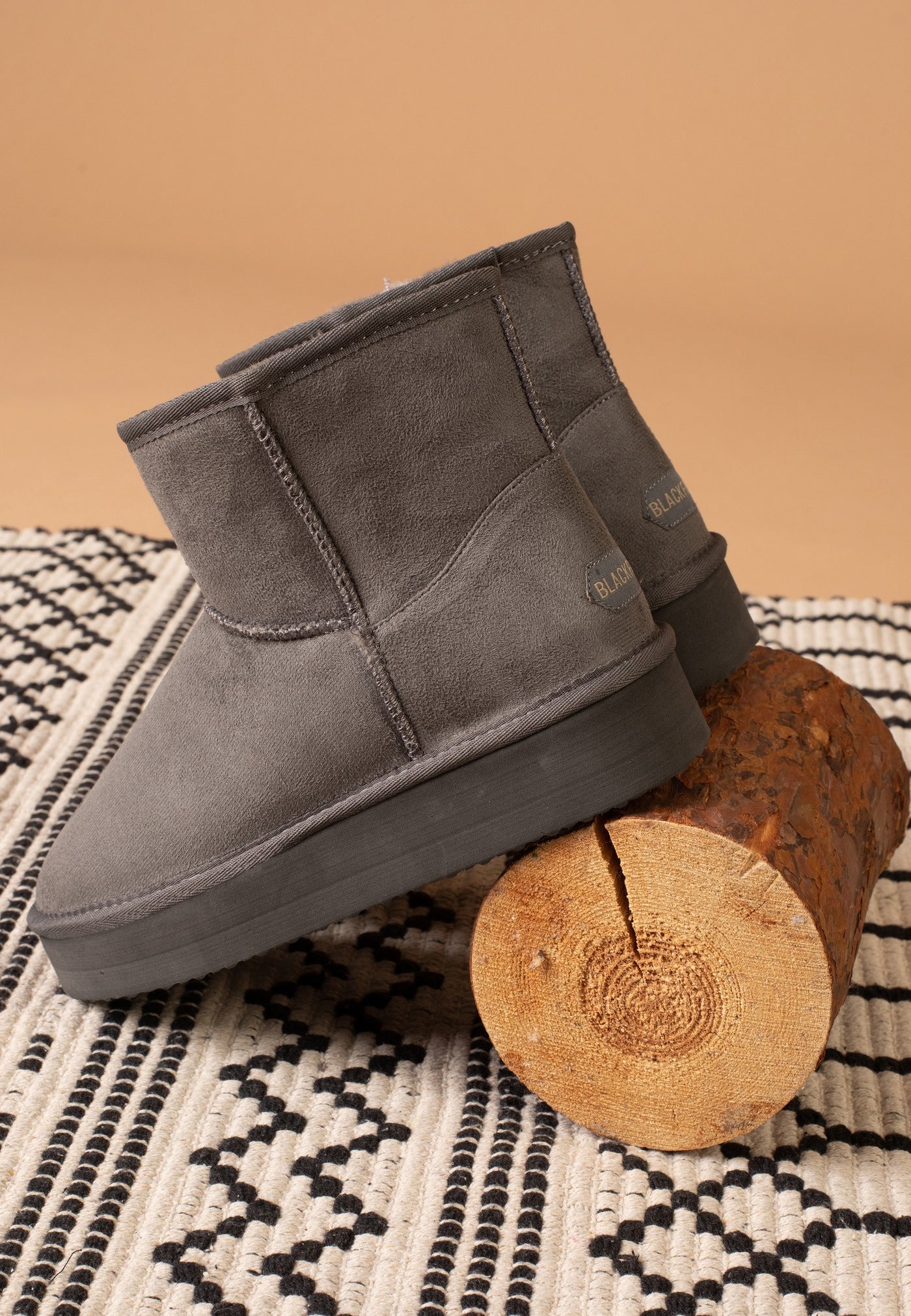 Bottine fourrée Princesse anthracite appuyée sur une bûche, vue de dessus du tapis ocre
