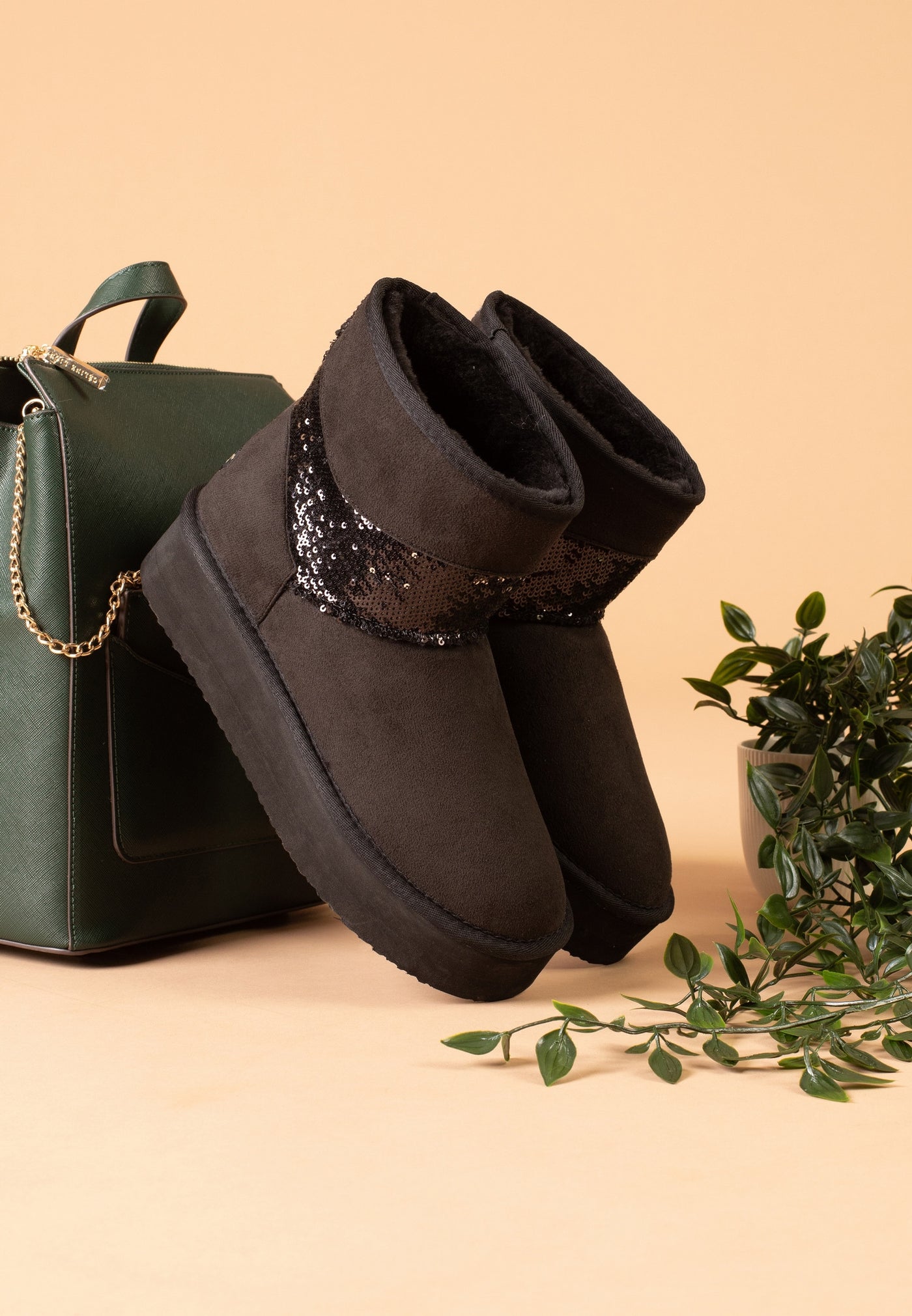 Paire de bottines fourrées Garthage noires posées de trois-quarts près d'un sac vert