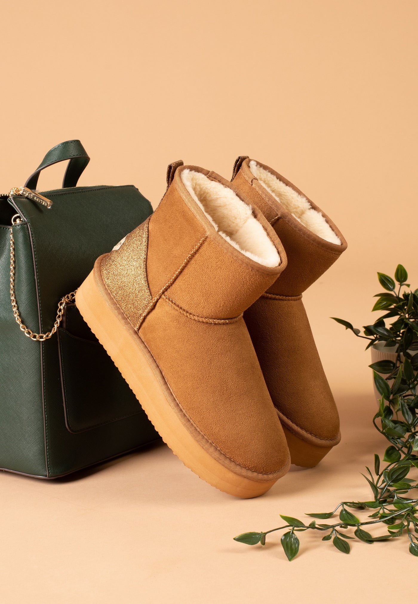 Paire de bottines fourrées Casablanca camel posée contre un sac vert, fond abricot