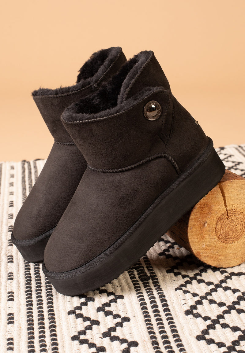 Bottines fourrées Cayuga noires vues de trois-quarts sur un tapis tissé noir et écru