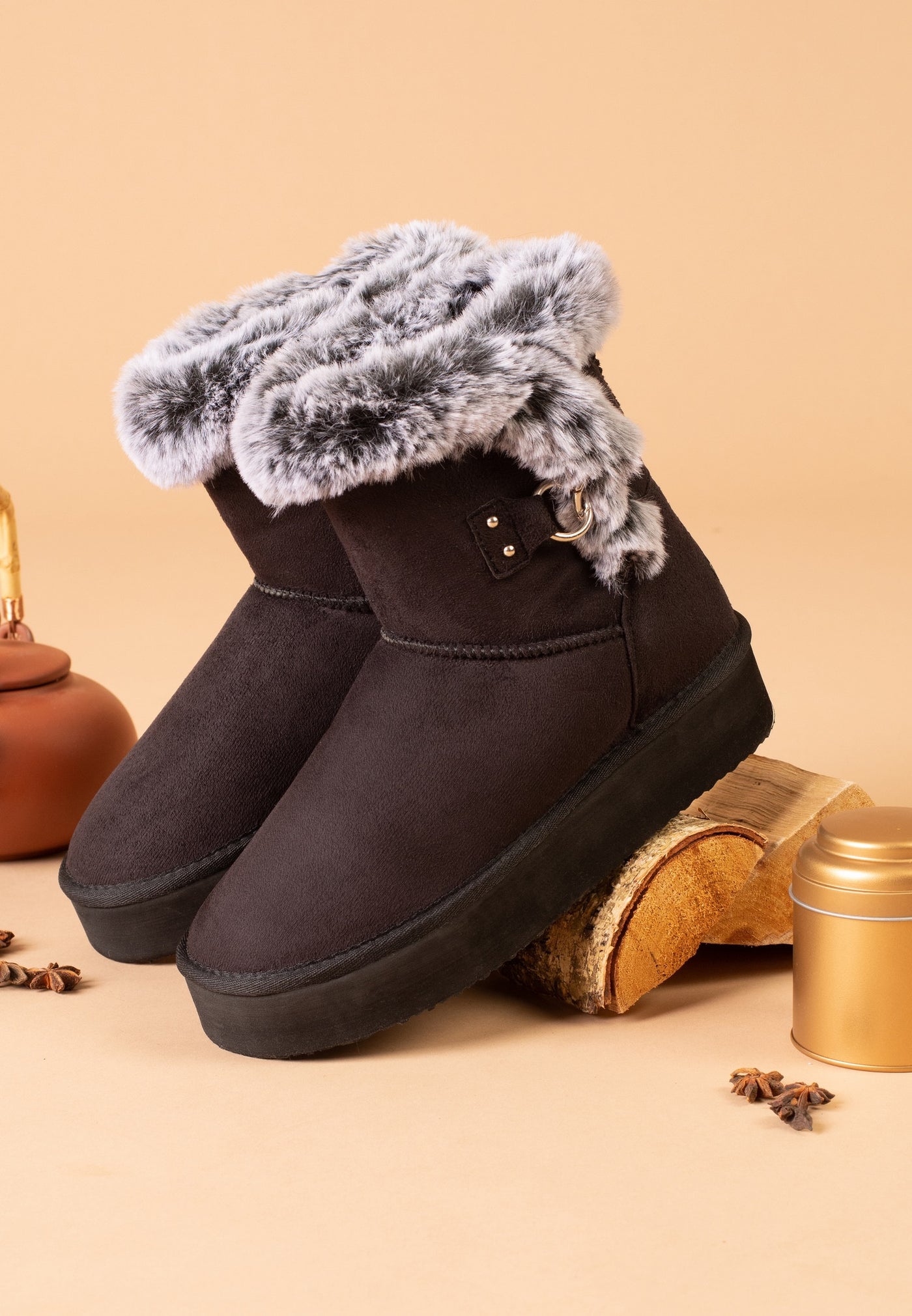 Paire de bottines fourrées Reindeer noires posée près d'une bûche et d'une boîte
