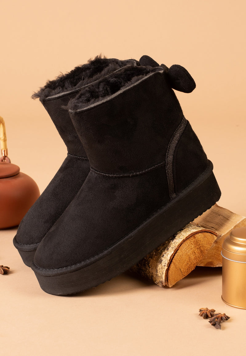 Bottines fourrées Champlain noires vues de trois-quarts contre une bûche, fond pêche
