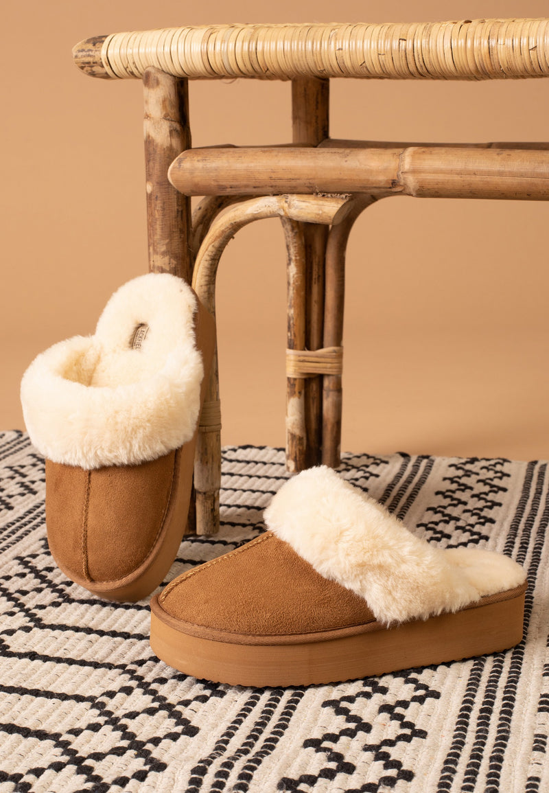 Paire de chaussons fourrés camel Sleepers Emilija posée sur un tapis à motifs