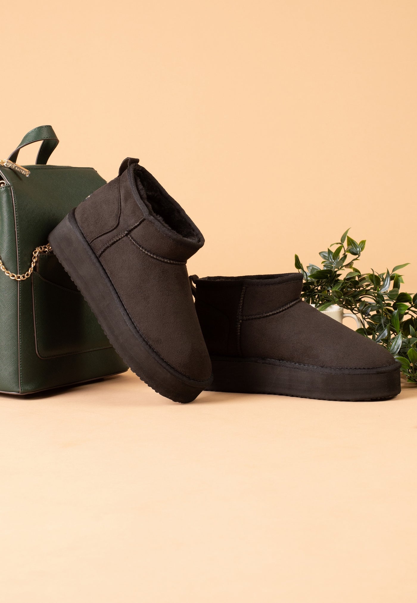 Bottines fourrées Milli noires posées de profil près d'un sac kaki et d'un feuillage
