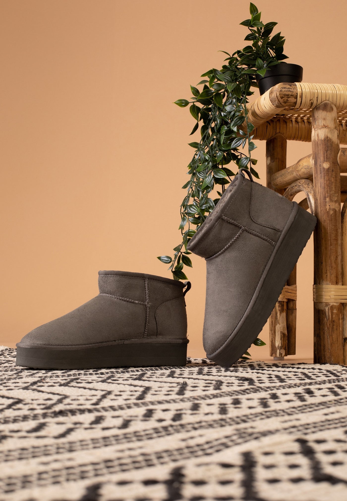 Deux bottines fourrées Milli anthracite vues de trois-quarts devant un tabouret de bambou