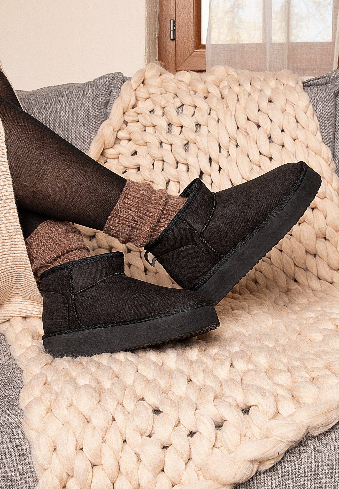 Pieds chaussés de bottines fourrées Milli noires, portées sur un plaid écru