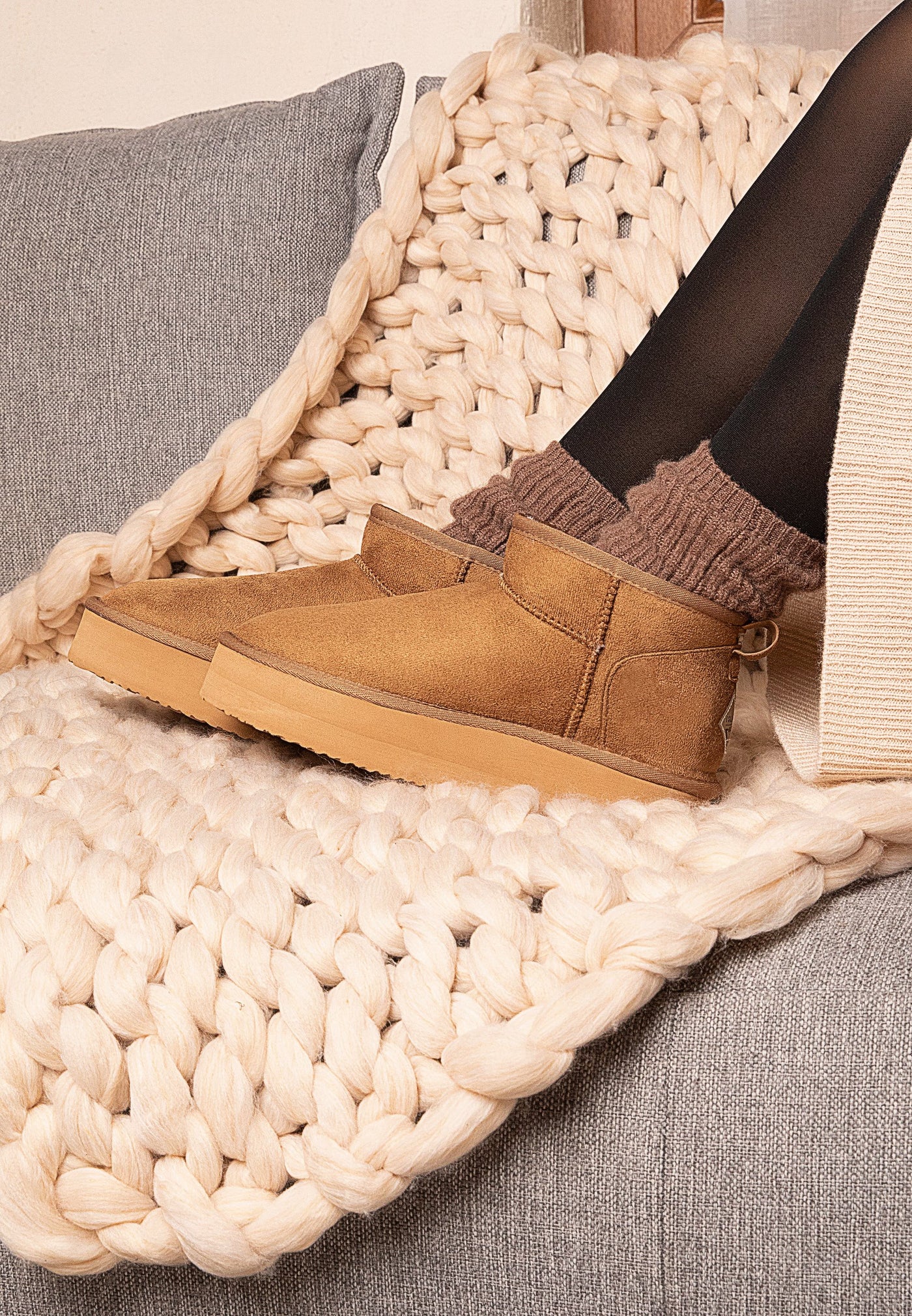 Bottines fourrées Milli camel portées sur un canapé, plaid en grosse maille écrue