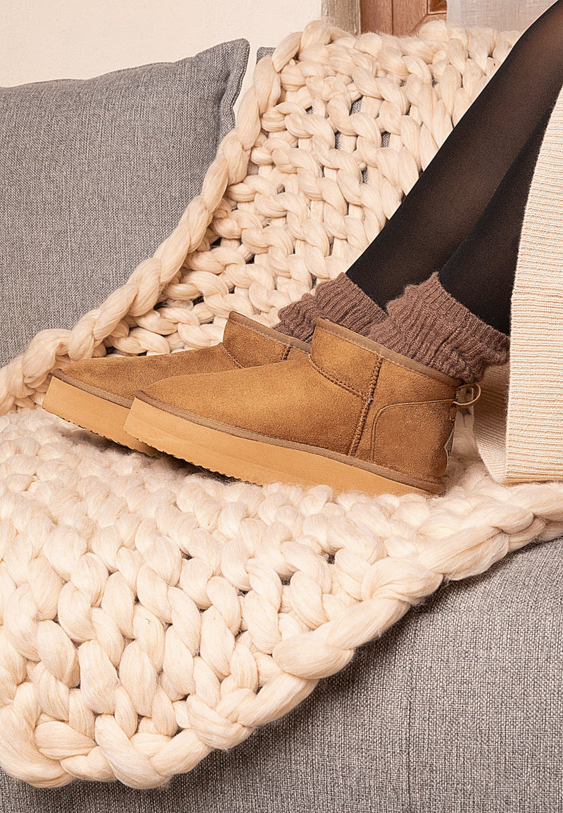 Bottines fourrées Milli camel portées sur un canapé, plaid en grosse maille écrue