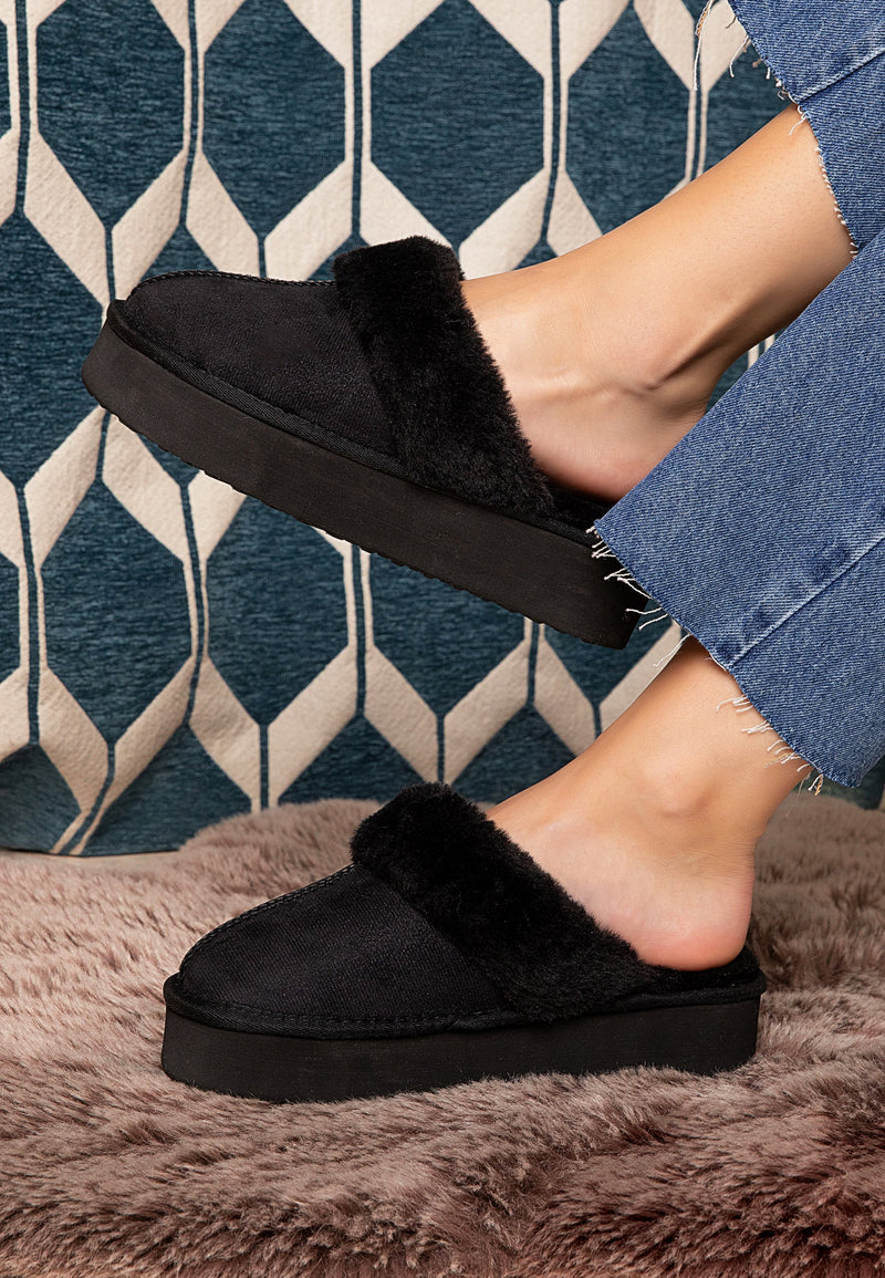 Chausson fourré noir Sleepers Emilija de profil, pieds nus, jean et plaid rose derrière