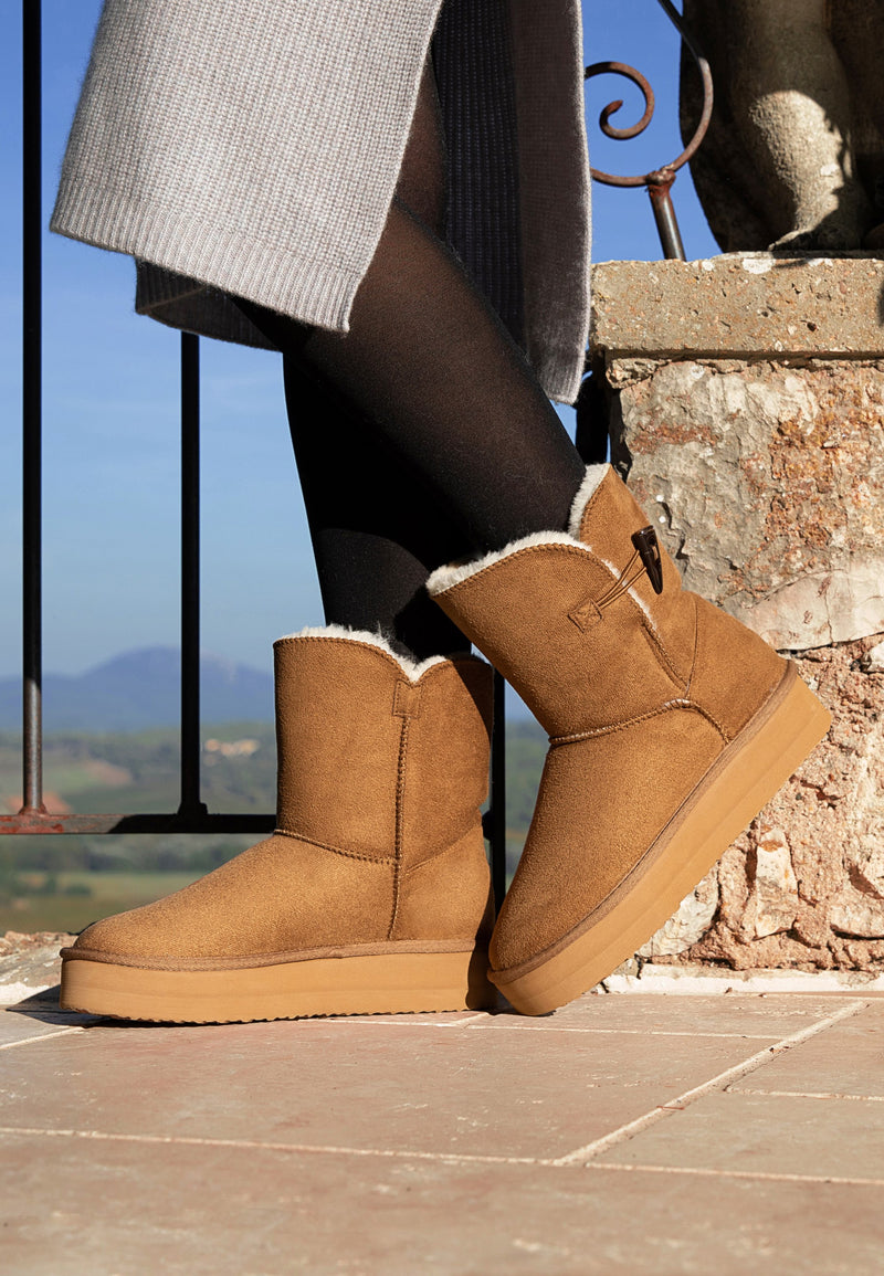 Bottines fourrées à plateforme Anais camel portées en extérieur, jupe grise et collants