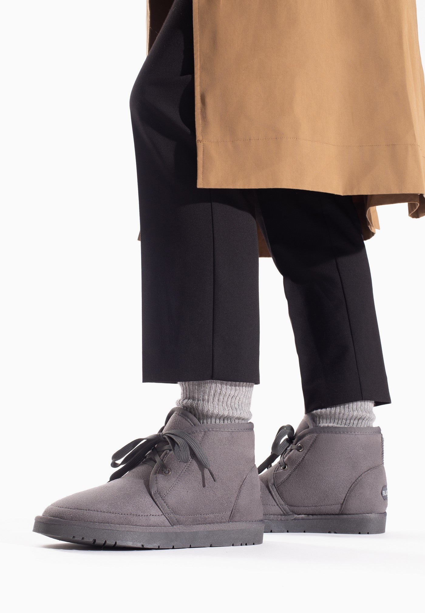 Bottines fourrées Chanel gris foncé portées avec un pantalon noir et un trench camel