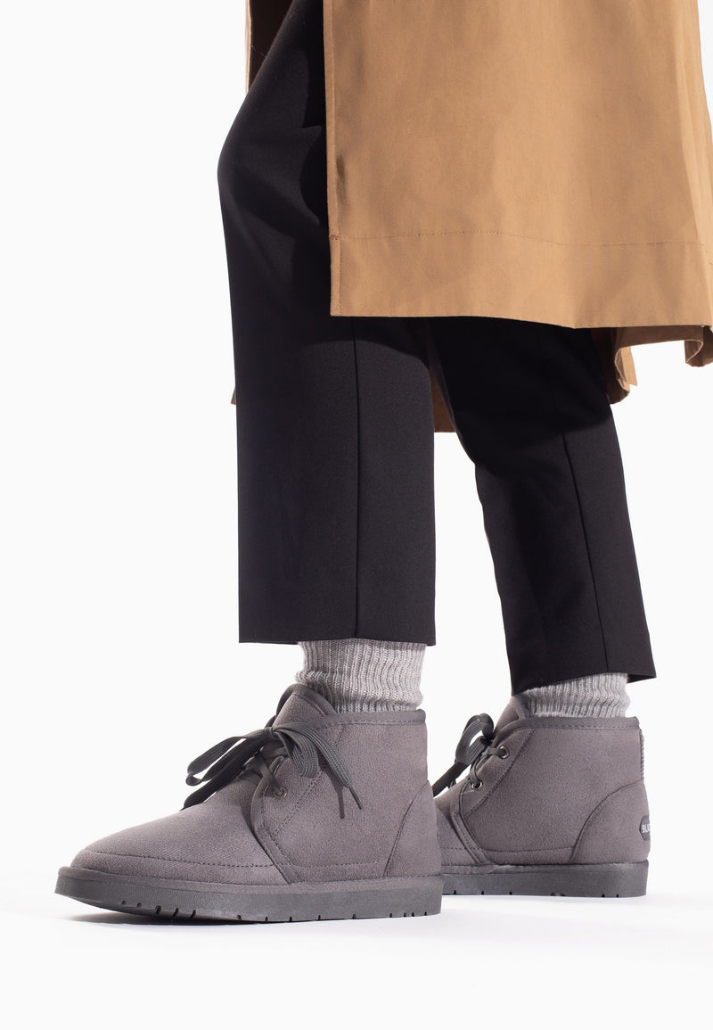 Bottines fourrées Chanel gris foncé portées avec un pantalon noir et un trench camel