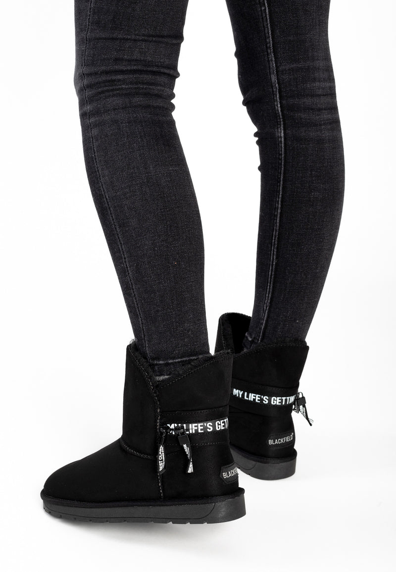 Bottines fourrées Zeek noires portées avec un jean gris, rubans imprimés visibles