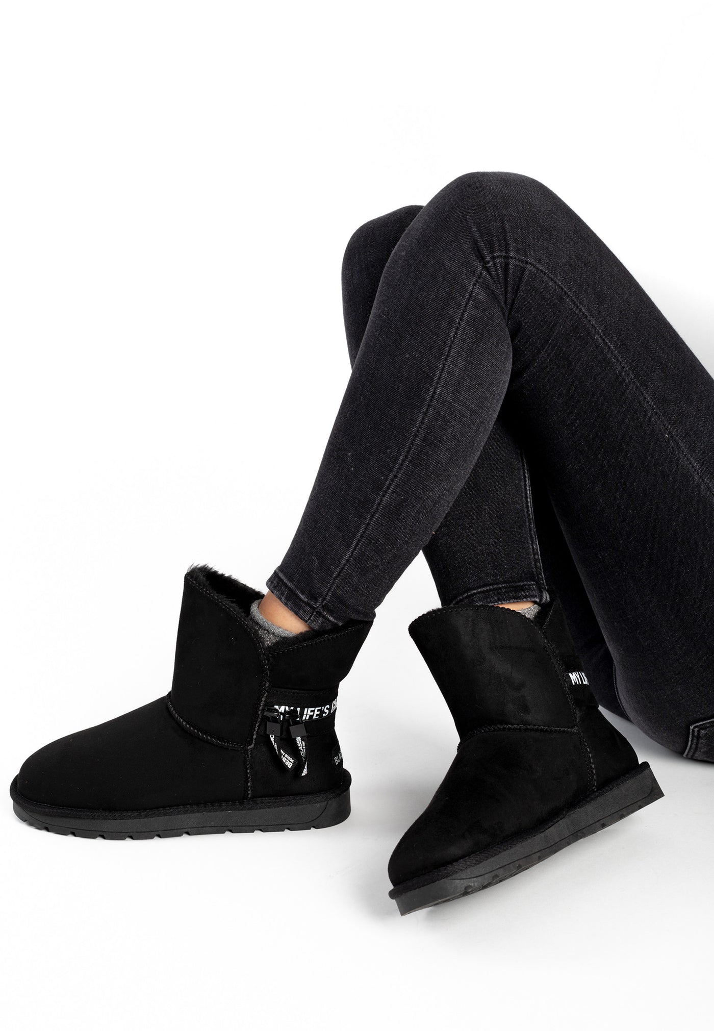 Bottines fourrées Zeek noires portées jambes croisées, semelle de la botte levée