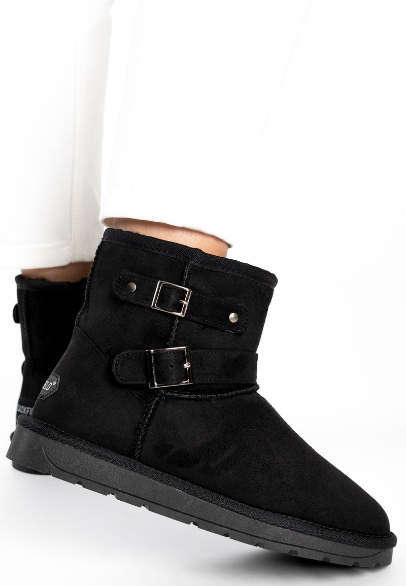 Bottine fourrée Olwen noire portée de près, boucle argentée et pantalon blanc