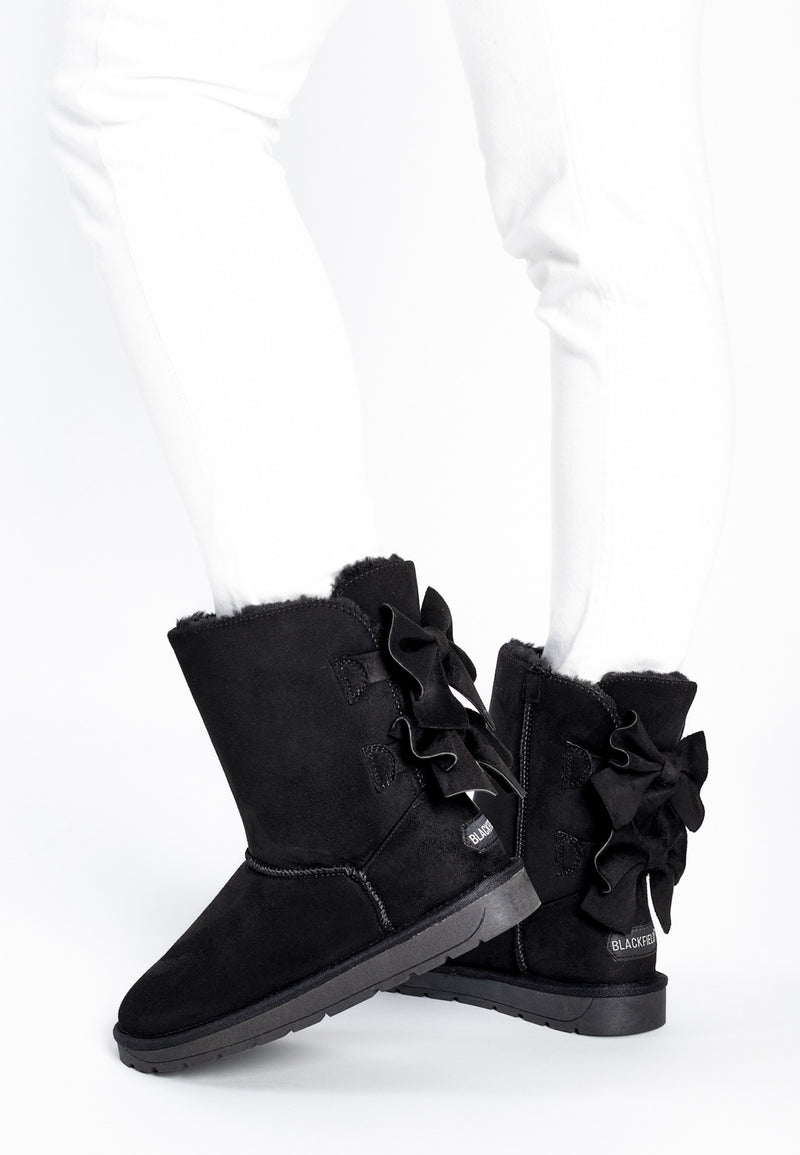 Bottines fourrées Livai noires portées avec un jean blanc, nœuds derrière le talon