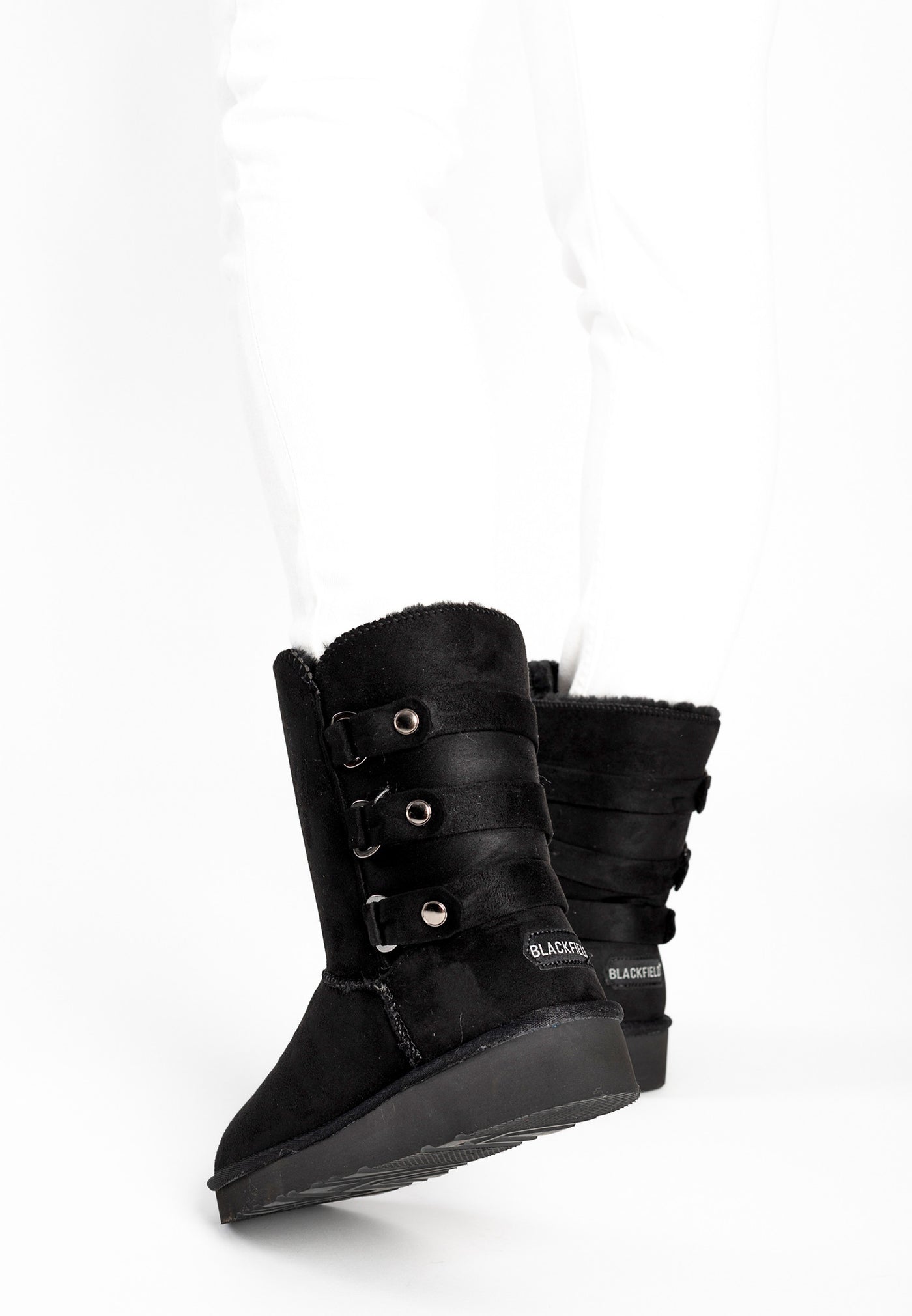 Bottes fourrées Gena noires portées avec un jean blanc, trois pattes à boutons argentés