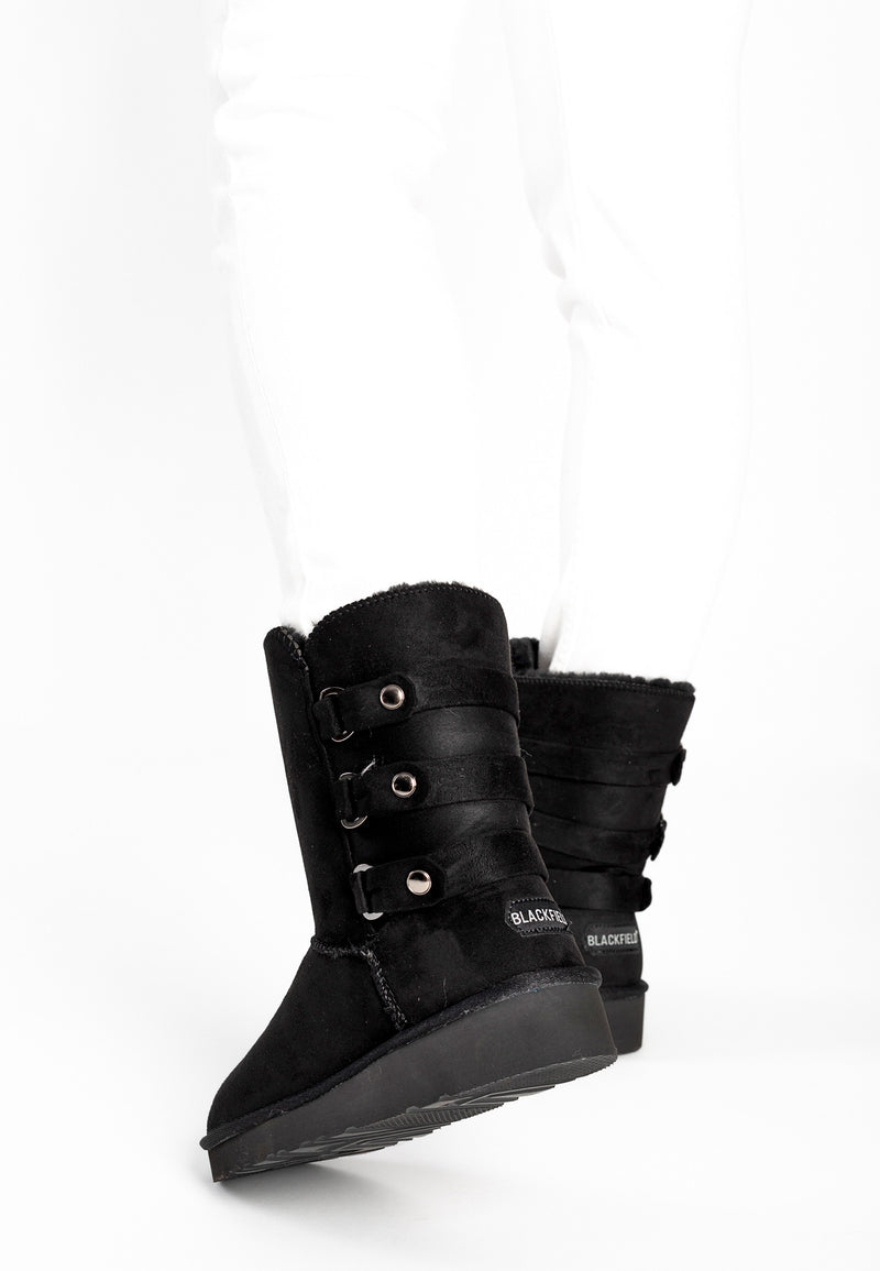 Bottes fourrées Gena noires portées avec un jean blanc, trois pattes à boutons argentés