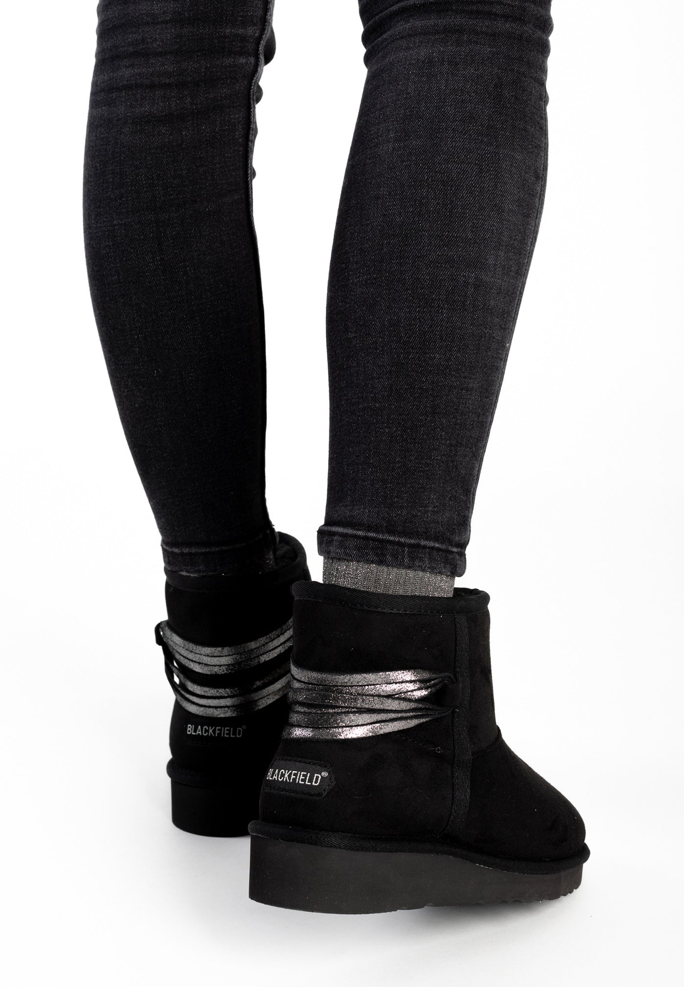 Bottines fourrées Dolce noires portées de dos avec un jean foncé, lanières argentées