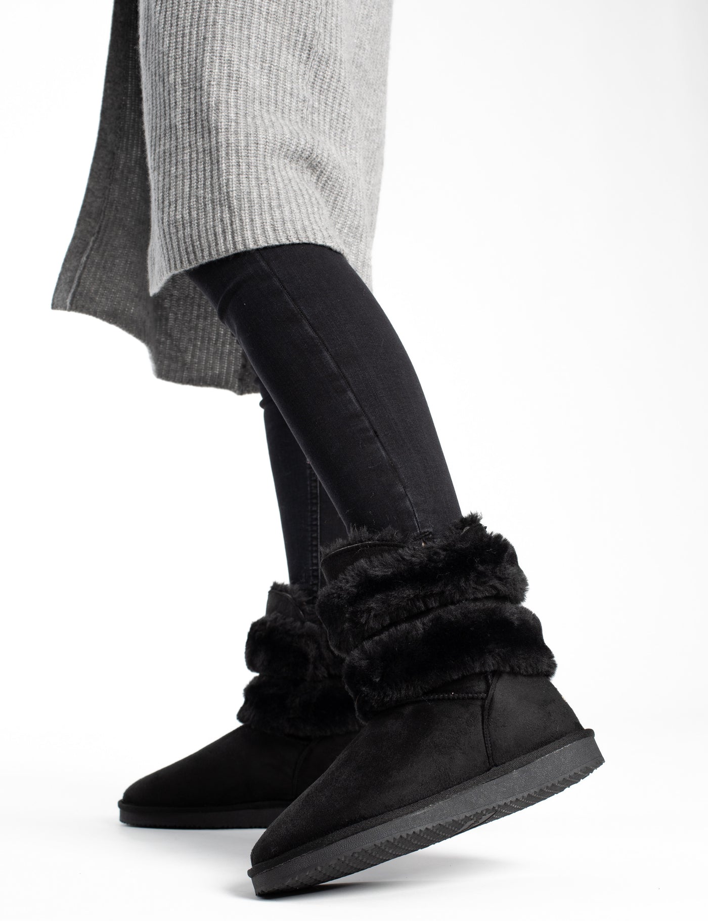 Bottines fourrées Erie noires en marche, jean noir et long gilet gris sur fond blanc