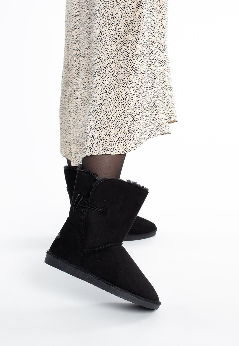 Bottines fourrées mi-mollet Anais noires portées en marche avec une jupe imprimée écrue