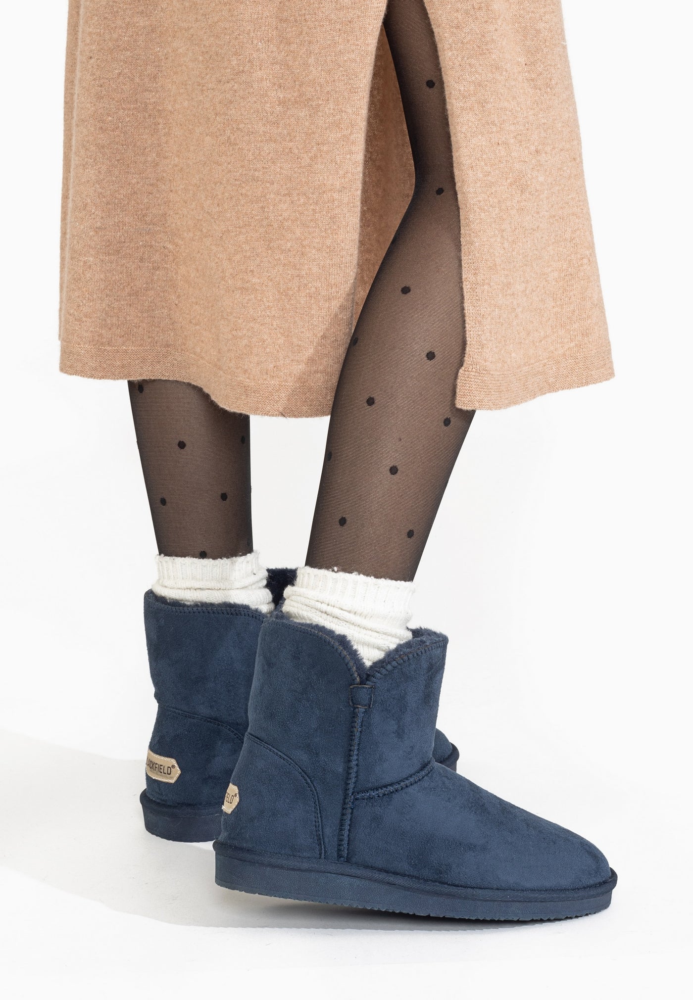 Bottines fourrées Bellevue marine portées de dos sous une jupe camel, talons marqués
