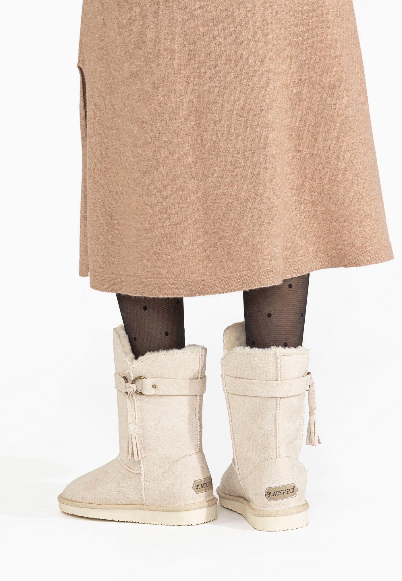 Bottes fourrées Greede naturel vues de dos sous une jupe camel, étiquettes aux talons
