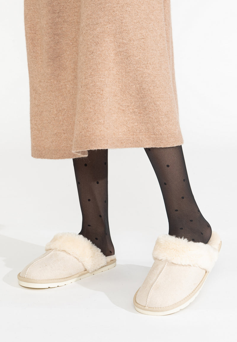 Chaussons fourrés Sleepers Emilija naturel vus de profil sous un manteau camel