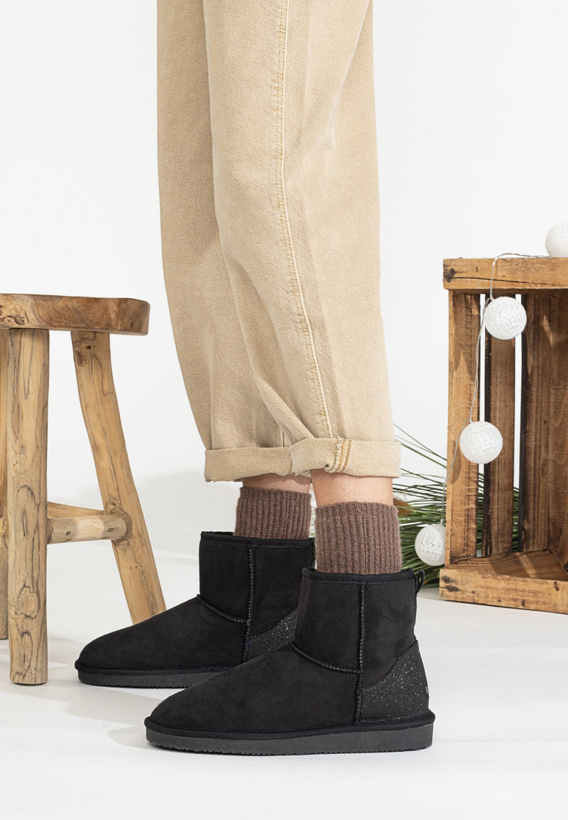 Bottines fourrées Casablanca noires portées près d'un tabouret en bois et d'une guirlande