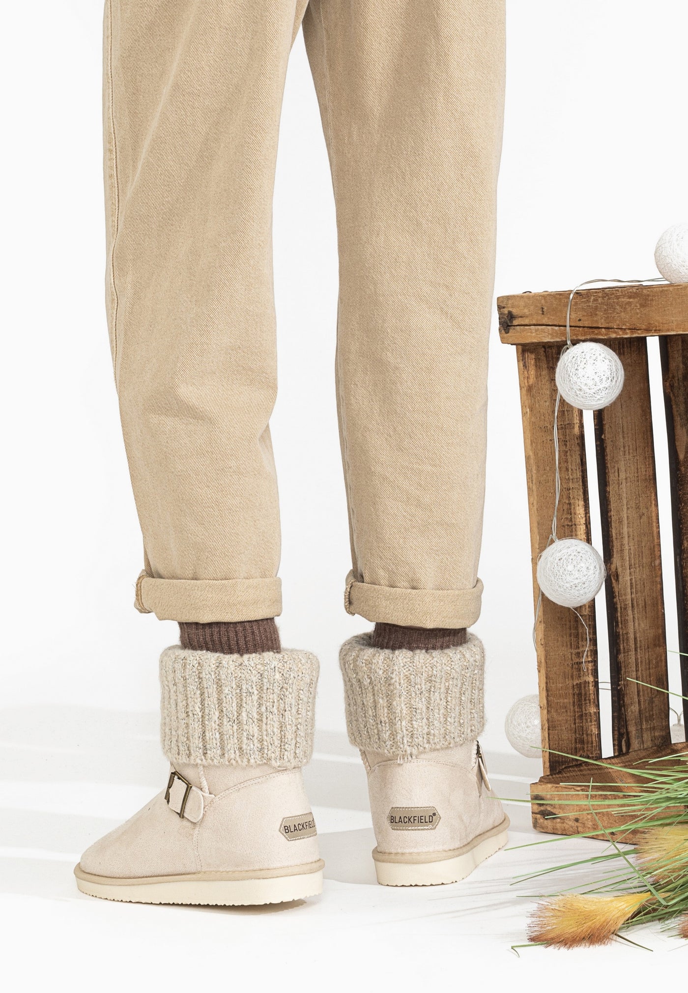 Bottines fourrées Kylie naturel portées de dos, pantalon beige et cageot de bois