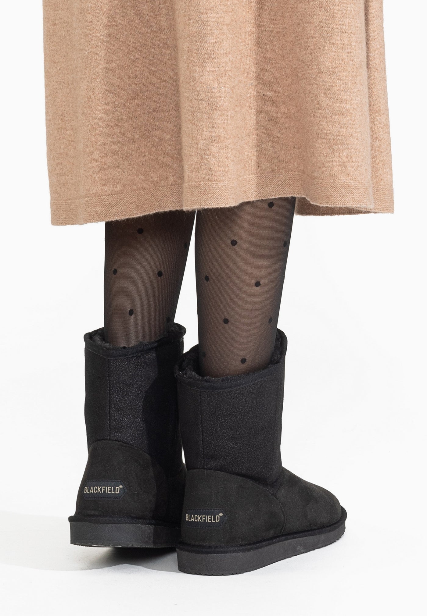 Bottines fourrées Clane noires portées de dos, jupe camel et collant à pois