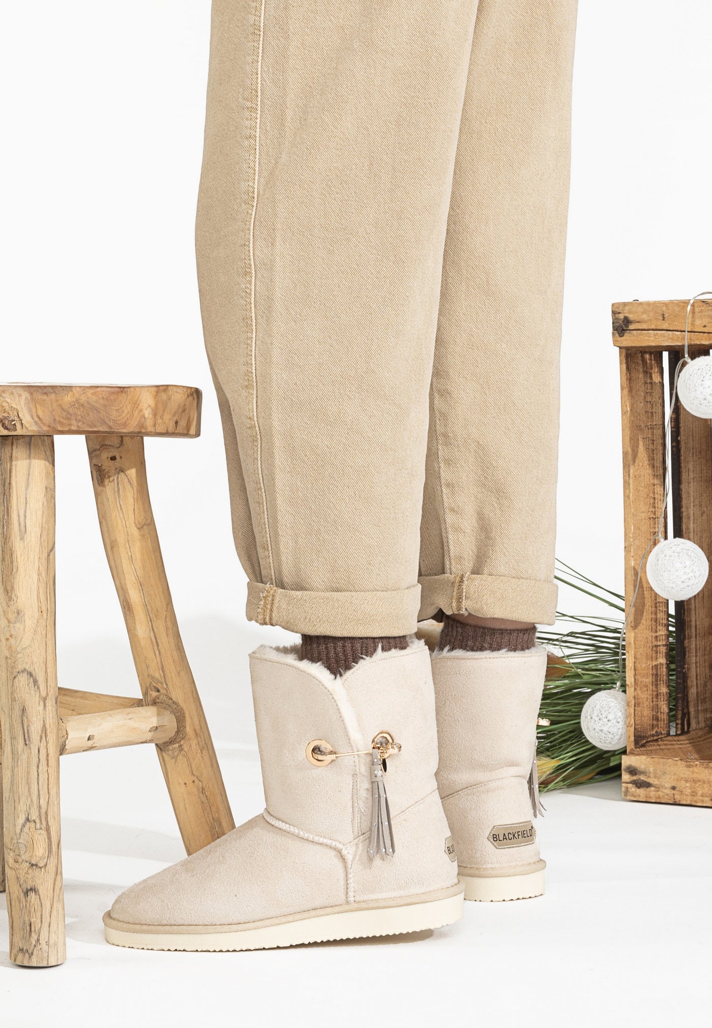 Bottines fourrées Clair naturel portées près d'un tabouret en bois, cols garnis