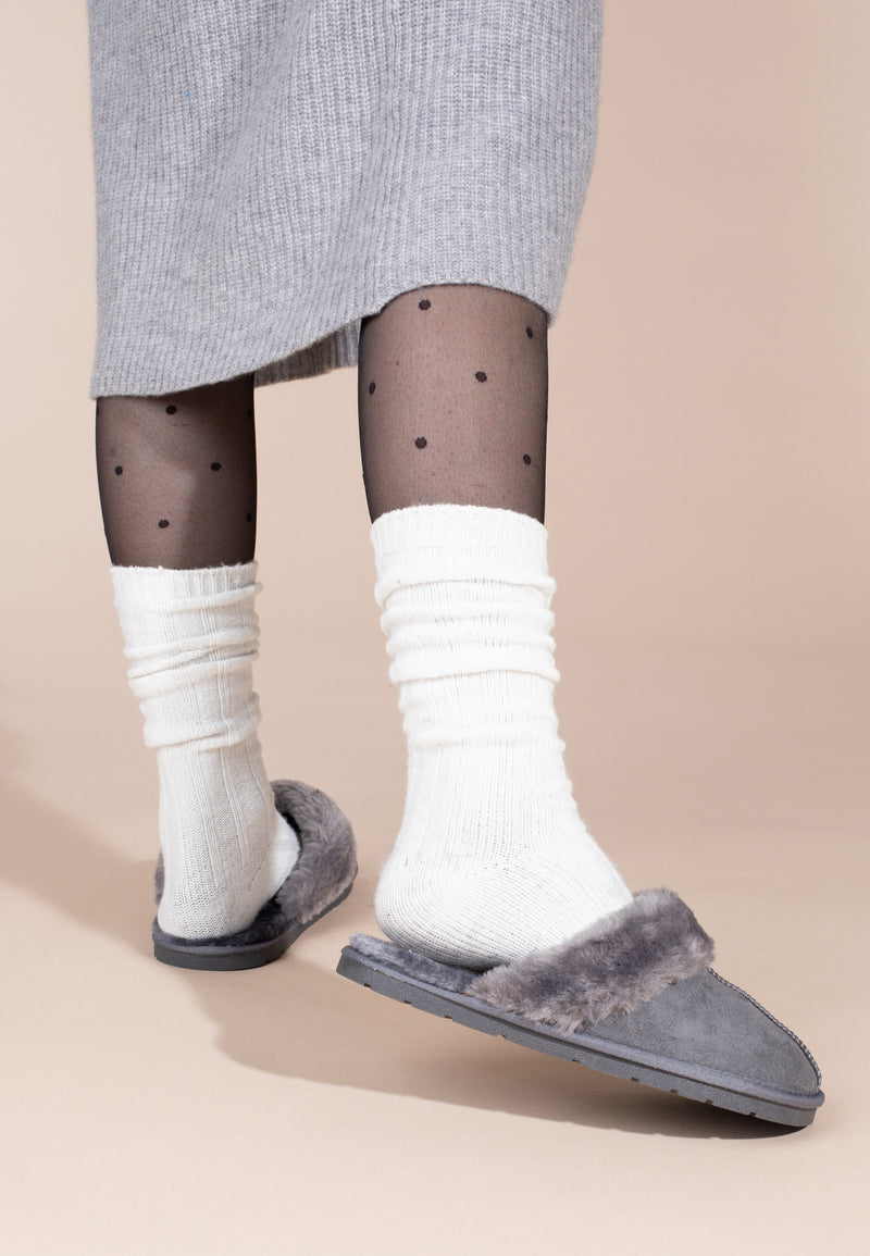 Aux pieds en chaussettes blanches, la paire de chaussons fourrés Sleepers Emilija gris foncé