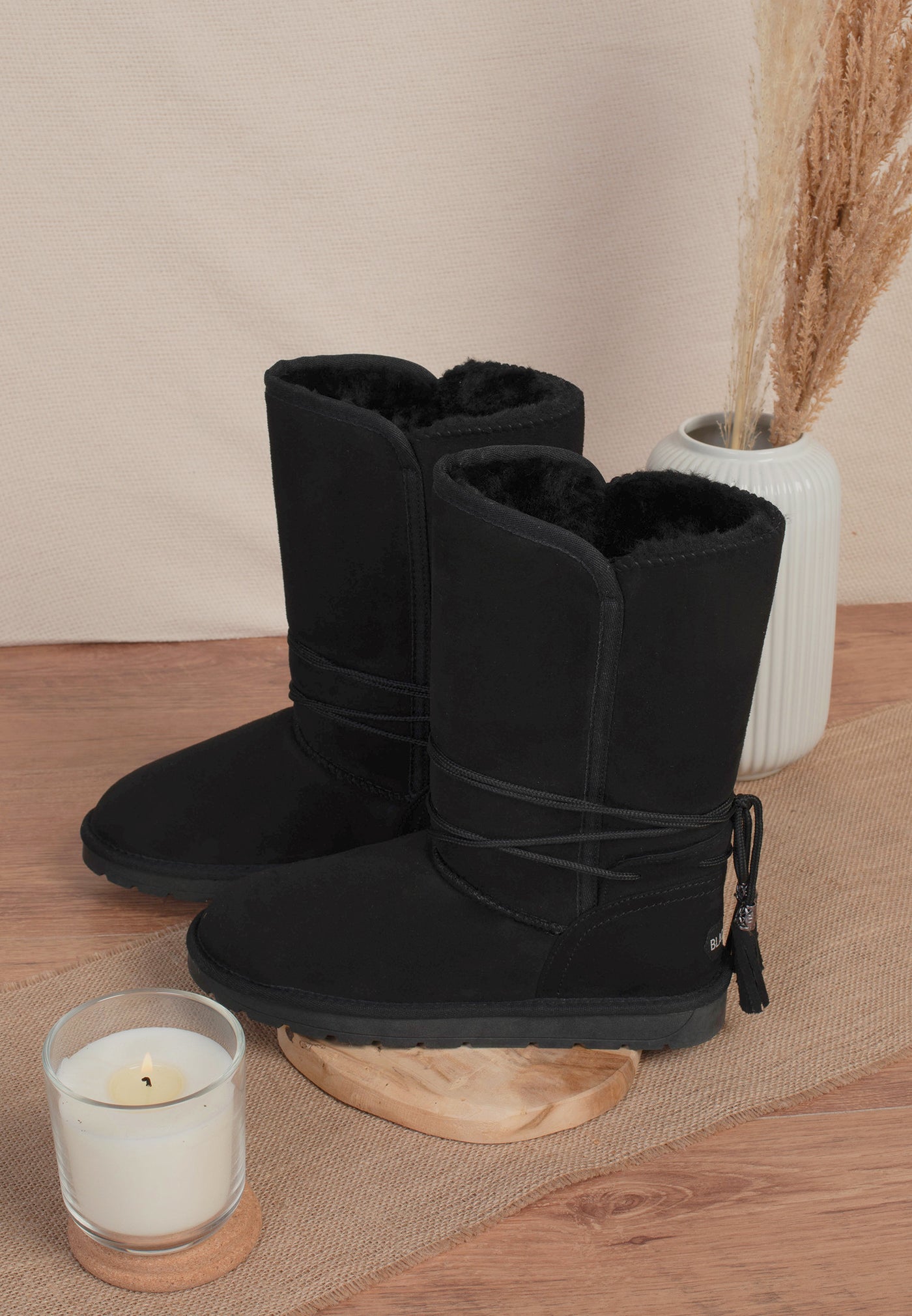 Paire de bottes fourrées Eowin noires posée près d'une bougie, doublure sombre visible au bord