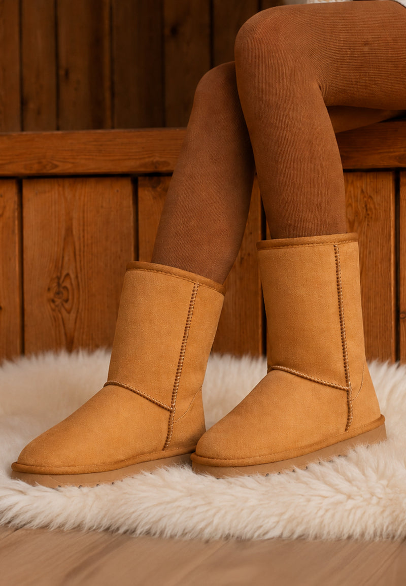 Bottes fourrées Joy camel portées avec des collants caramel sur un tapis clair
