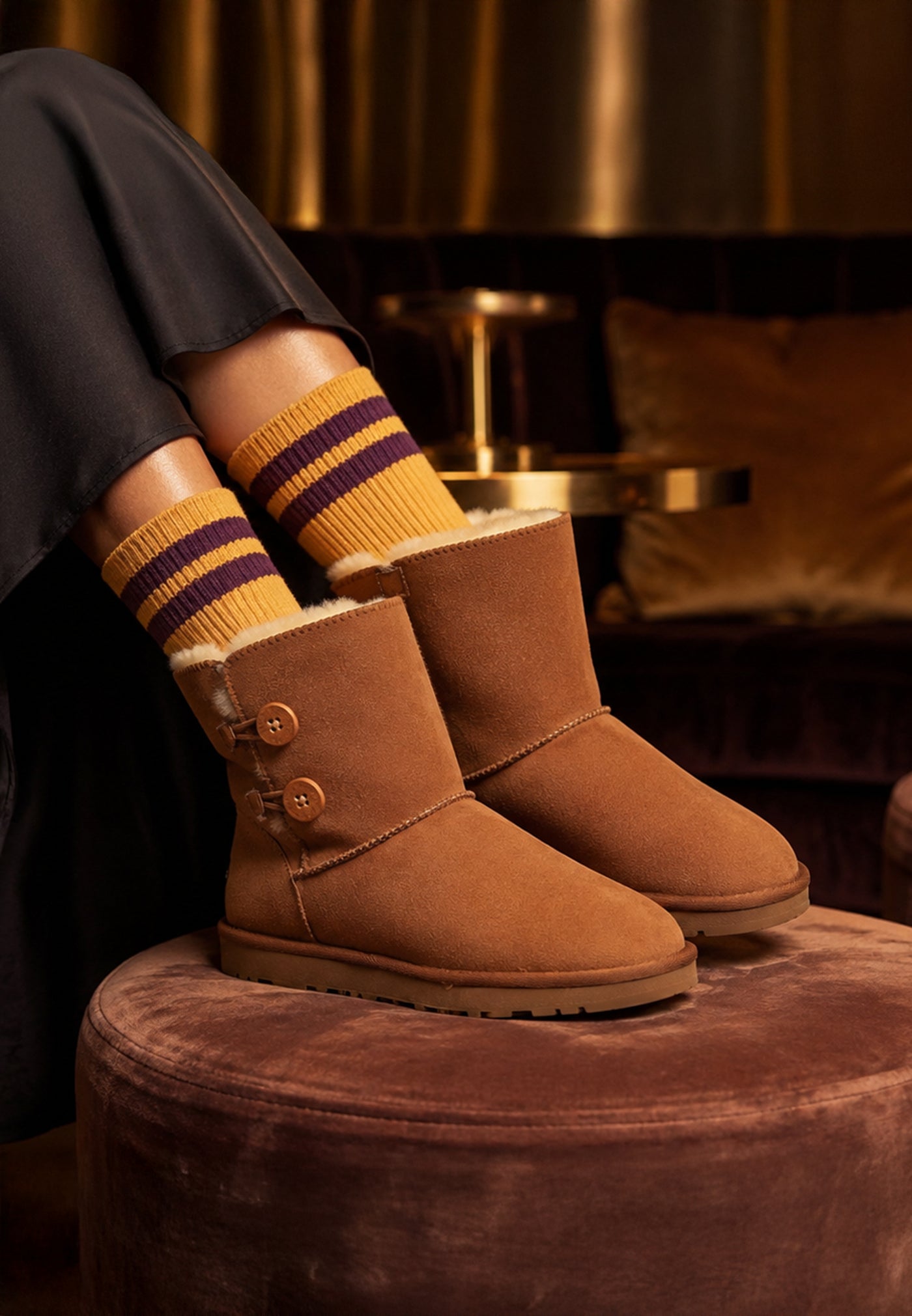 Bottines fourrées Lola camel portées avec des chaussettes rayées, posées sur un pouf