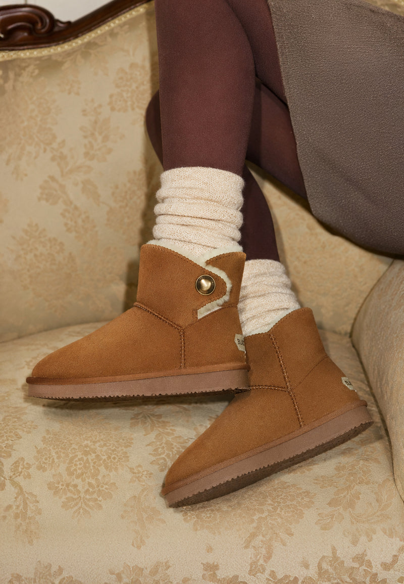 Bottines fourrées Cayuga camel portées avec des collants bordeaux sur un fauteuil