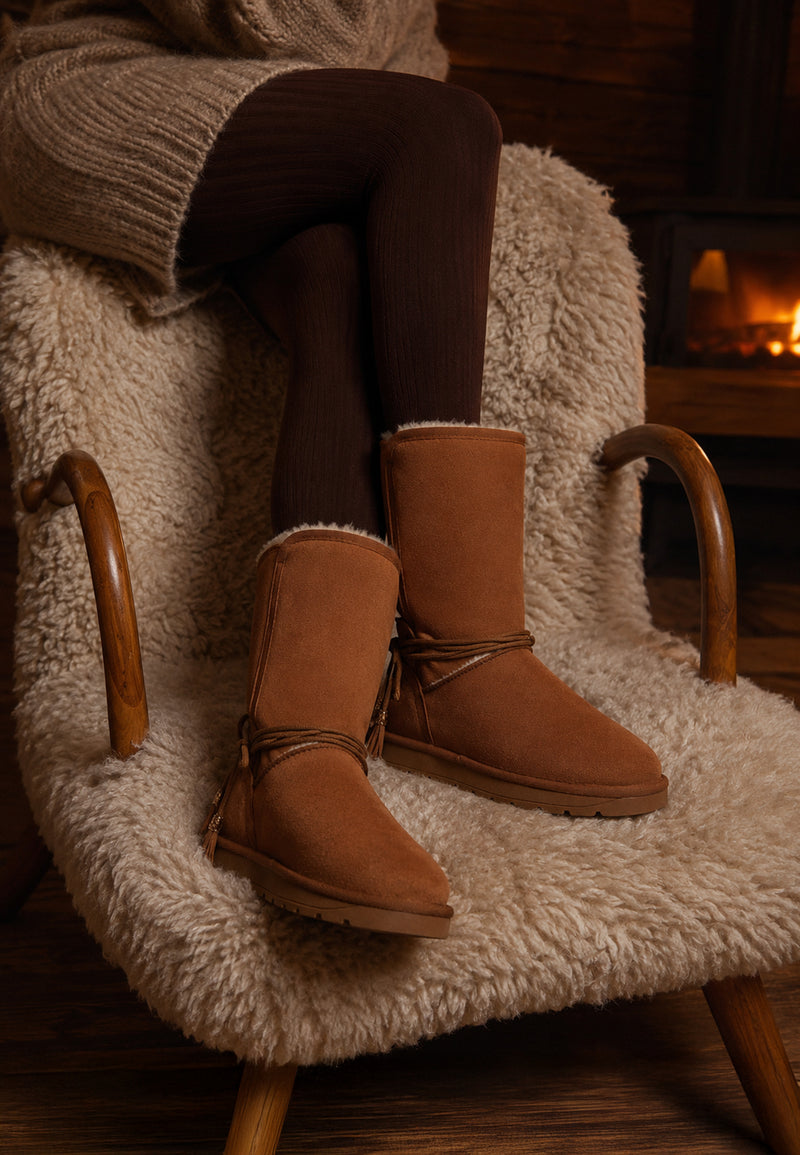 Bottes fourrées hautes Eowin camel portées dans un fauteuil, devant une cheminée