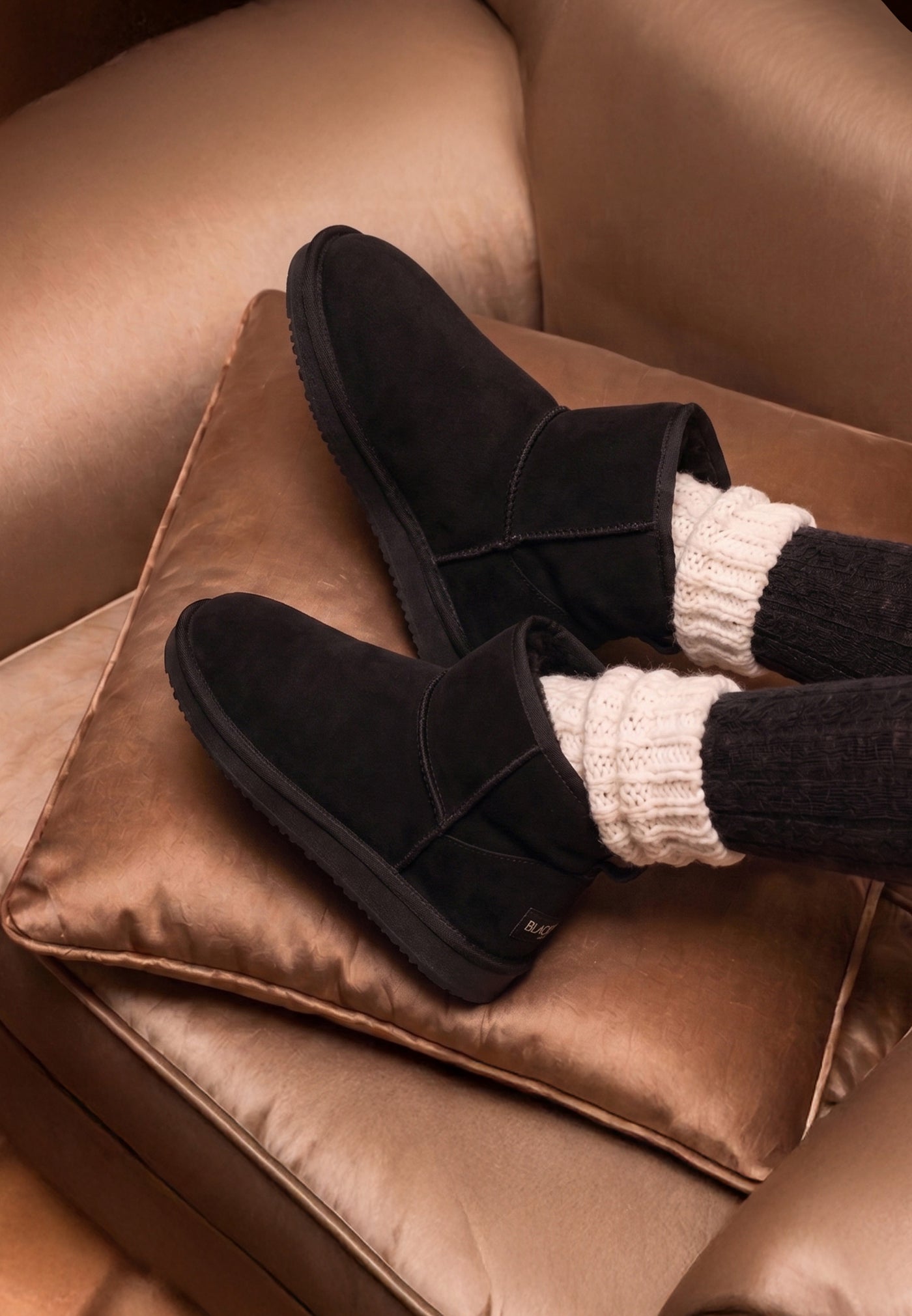 Bottines fourrées Princesse noires posées sur un coussin satiné, vues de trois-quarts