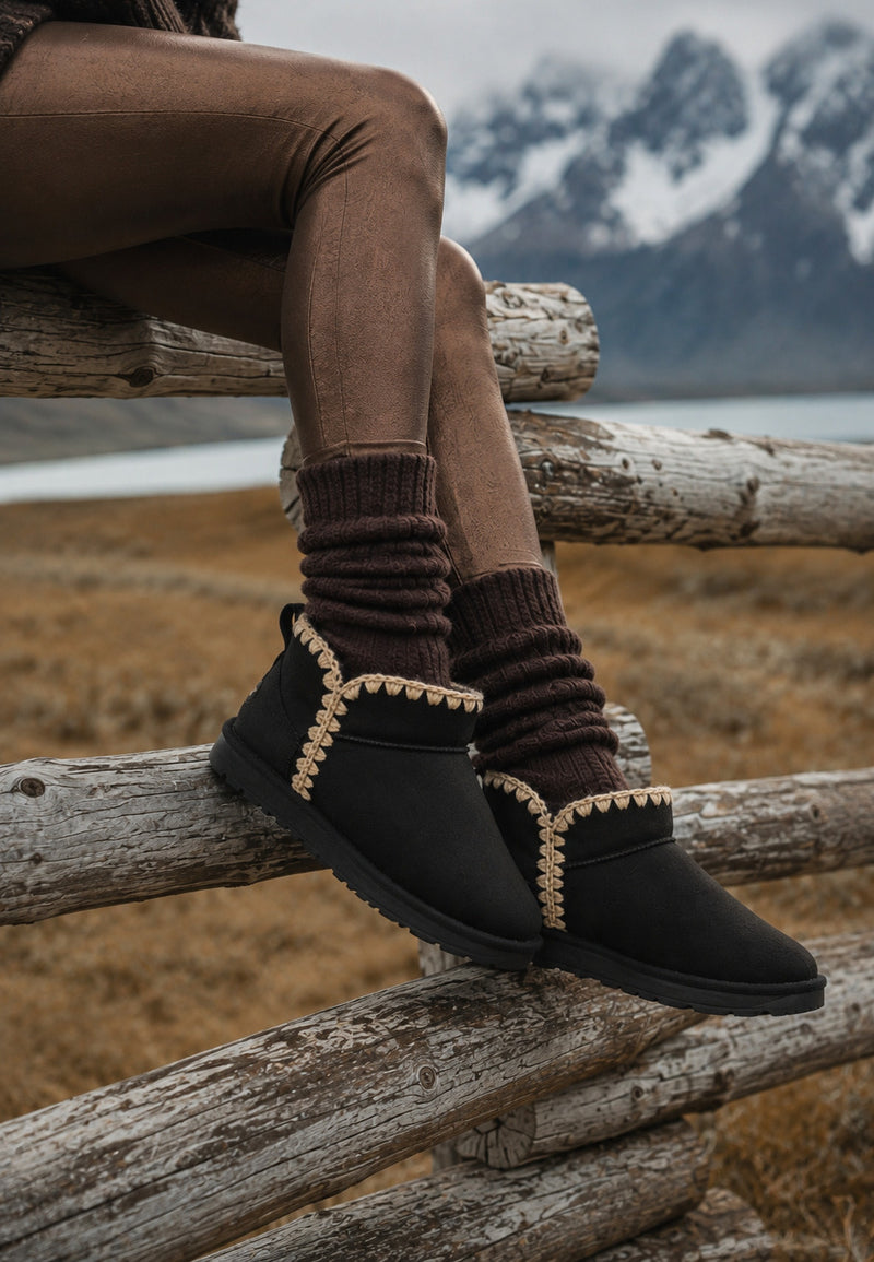 Bottines fourrées Bakelite noires portées sur une barrière de rondins en montagne